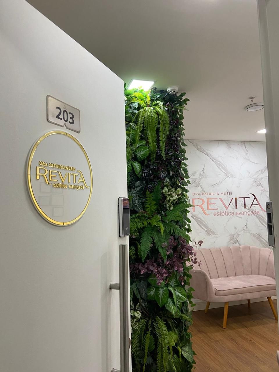 Entrada da Revita na sala 203, com o logo na porta, jardim vertical e a recepção ao fundo.